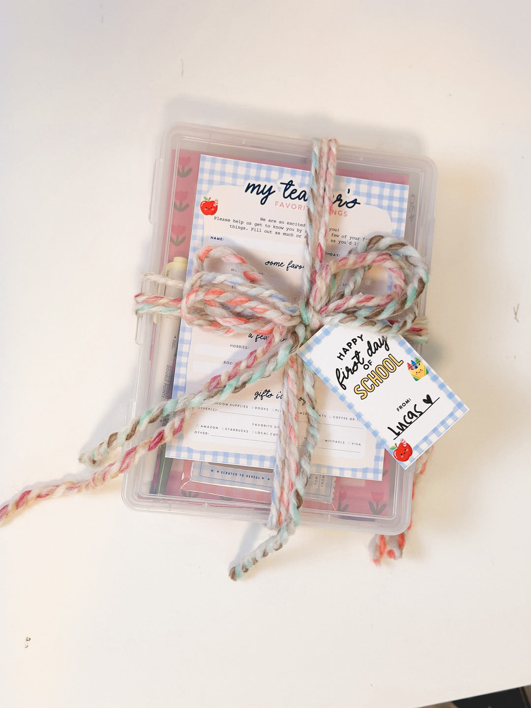 A clear plastic storage box tied with a pastel multicolor yarn bow and a 'Happy First Day at School' tag, containing printed school-themed cards on a white background.
Printable Teacher Favorite Things questionnaire and Classroom Wishlist cards for planning personalized teacher gifts.