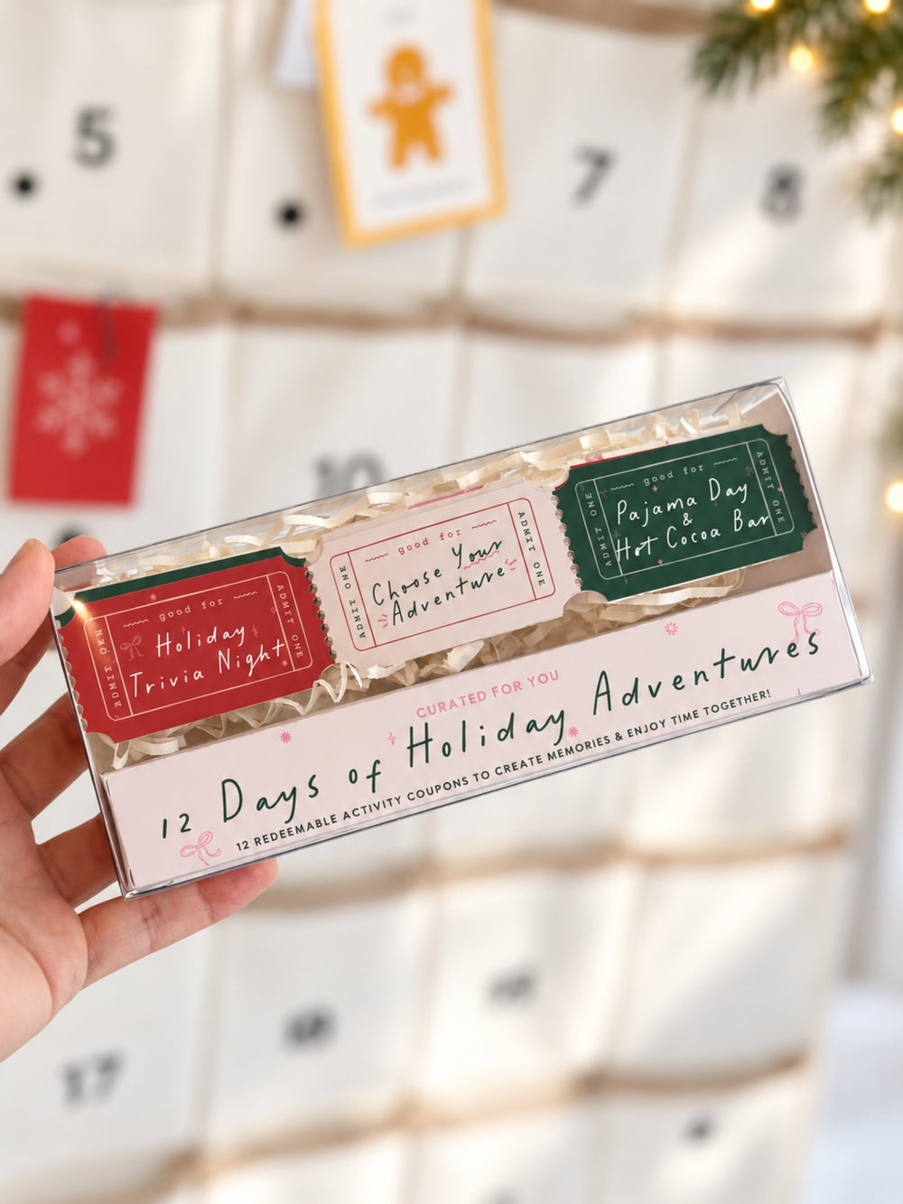 A hand holds a clear plastic box containing three holiday-themed activity coupon tickets against a blurred Christmas advent calendar background.