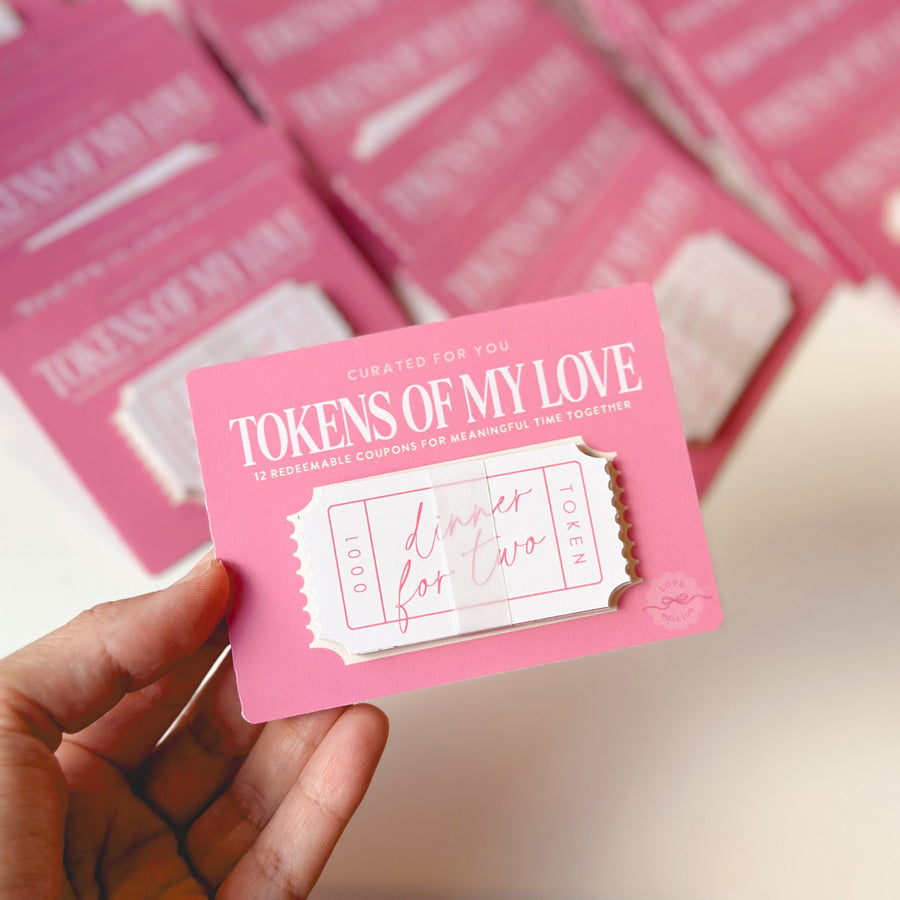 Hand holding a pink Valentine’s Day love coupon card with a “Dinner for Two” token, part of a romantic experience gift for couples, with matching coupon sets in the background.