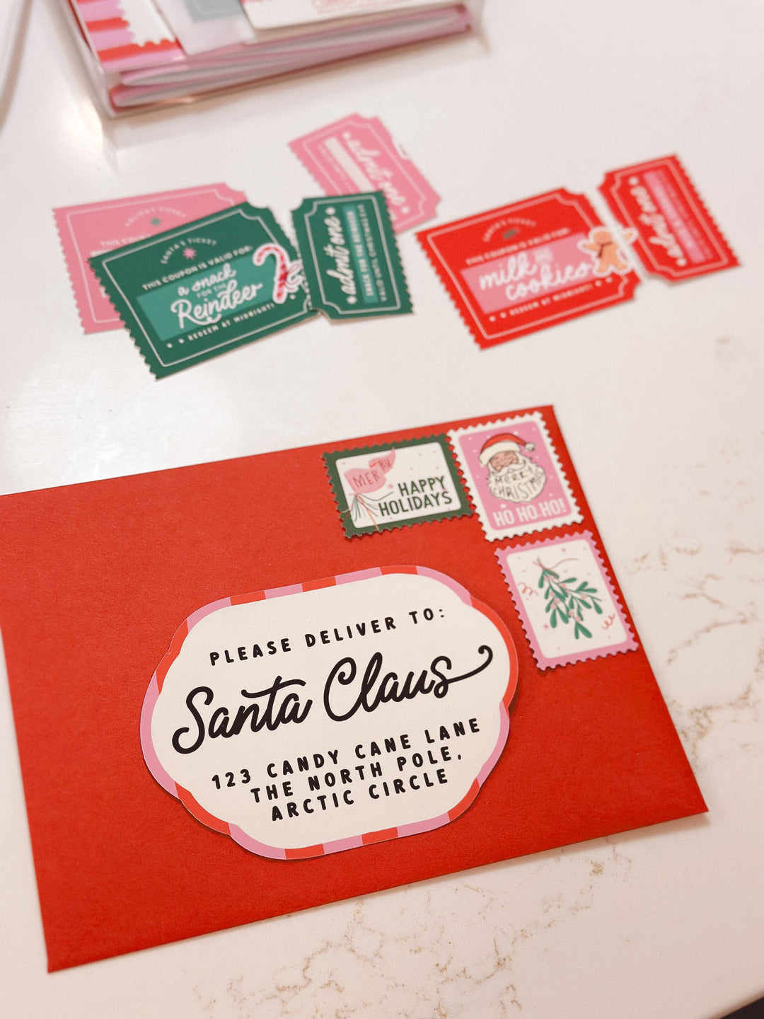 Red envelope with 'Please deliver to Santa Claus' text and decorative stamps on a white surface.